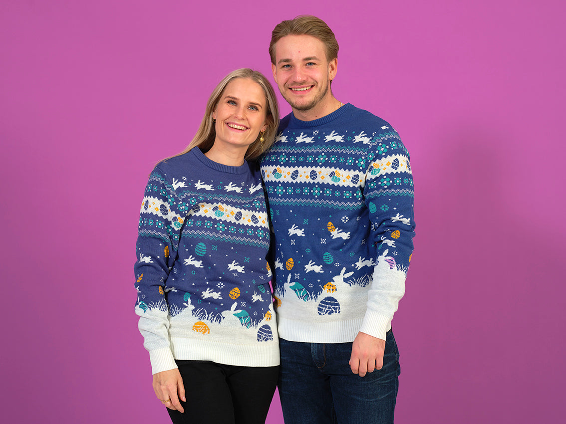 En mand og en dame poserer sammen i hver deres blå påskesweater.